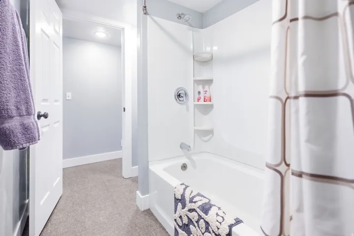 White tub and shower combination with chrome fixtures and built-in shelving