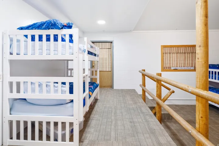 Multiple built-in bunk beds with slatted sides, wood-finish flooring, and natural wood railing