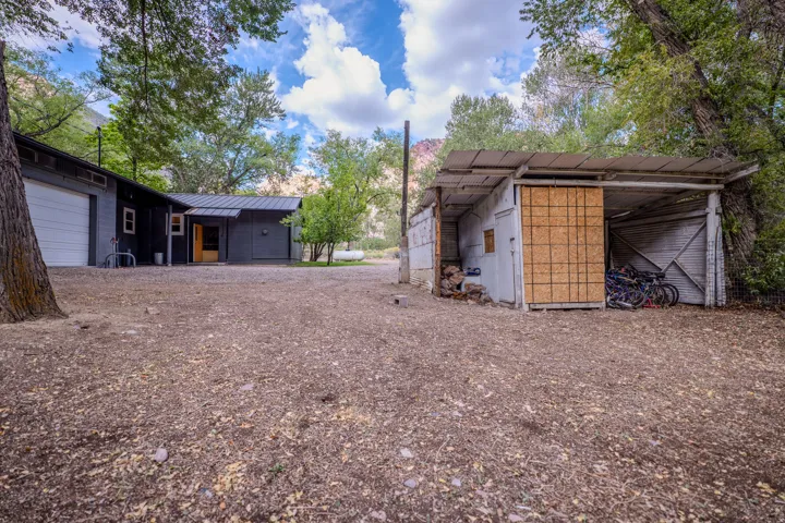 Detached garage with white overhead door, dark siding, covered entryway, and additional outbuilding with open storage