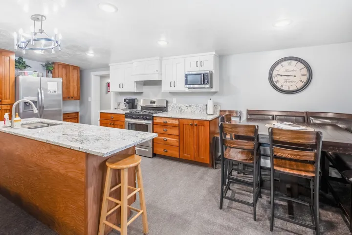 Kitchen featuring a central island with a sink, granite-style countertops, stainless steel appliances, and a gas range