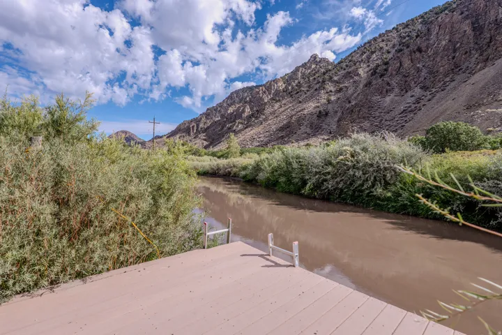 Deck with a river frontage, flanked by natural shrubbery and a prominent mountain backdrop