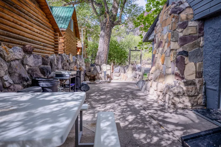 Log cabin exterior with a green metal roof, natural stone foundation, and concrete hardscaping