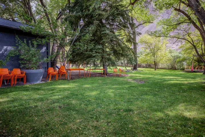 Expansive green lawn surrounded by mature trees, featuring a dark-toned building with a sloped roof