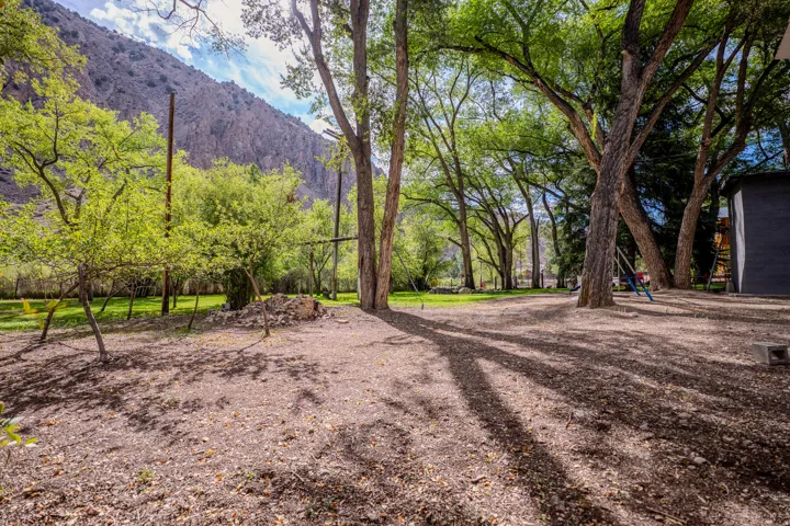 Mature tree-lined grounds with expansive gravel and lawn areas, backed by scenic mountain terrain