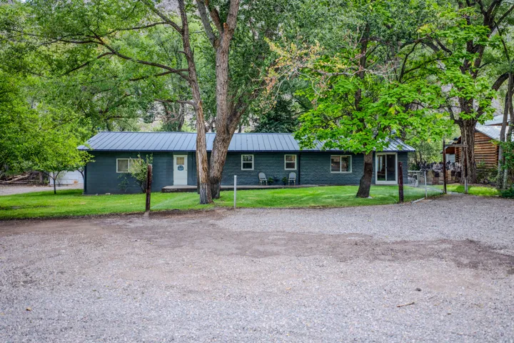 Gravel parking area, expansive green lawn, mature trees, dark exterior siding, and a metal roof