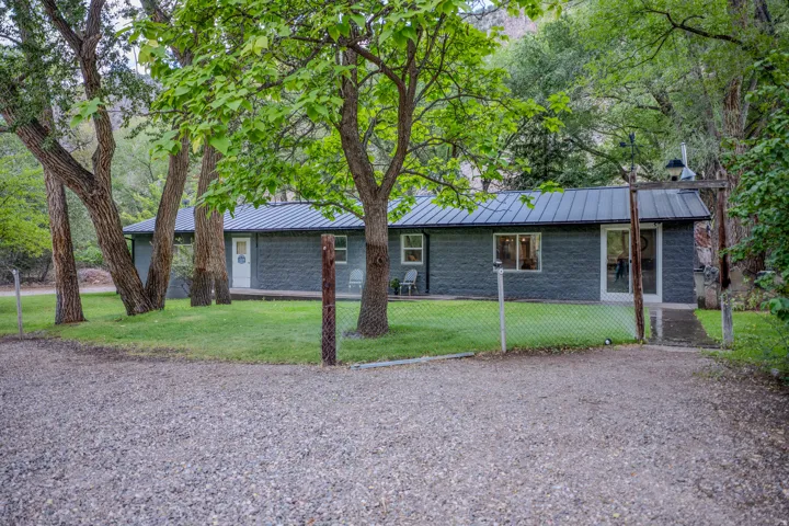 Gravel driveway leading to a residence featuring a dark metal roof, dark gray exterior siding, and multiple windows