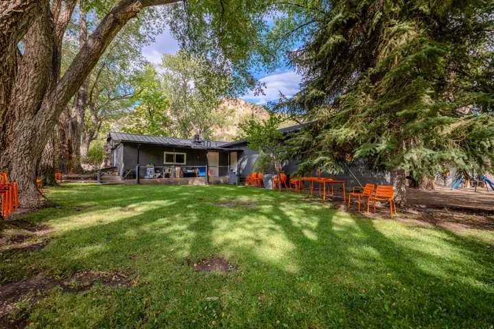 Spacious grassy area with mature shade trees and a dark-toned exterior structure with multiple windows