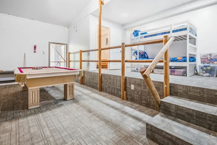 Recreational area featuring wood-look flooring, a stepped platform with integrated wood-look risers, and a rustic wood railing