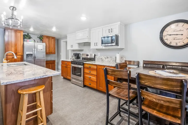 Kitchen featuring a central island with a sink, stainless steel appliances, white upper cabinetry, and wood-finish lower cabinetry