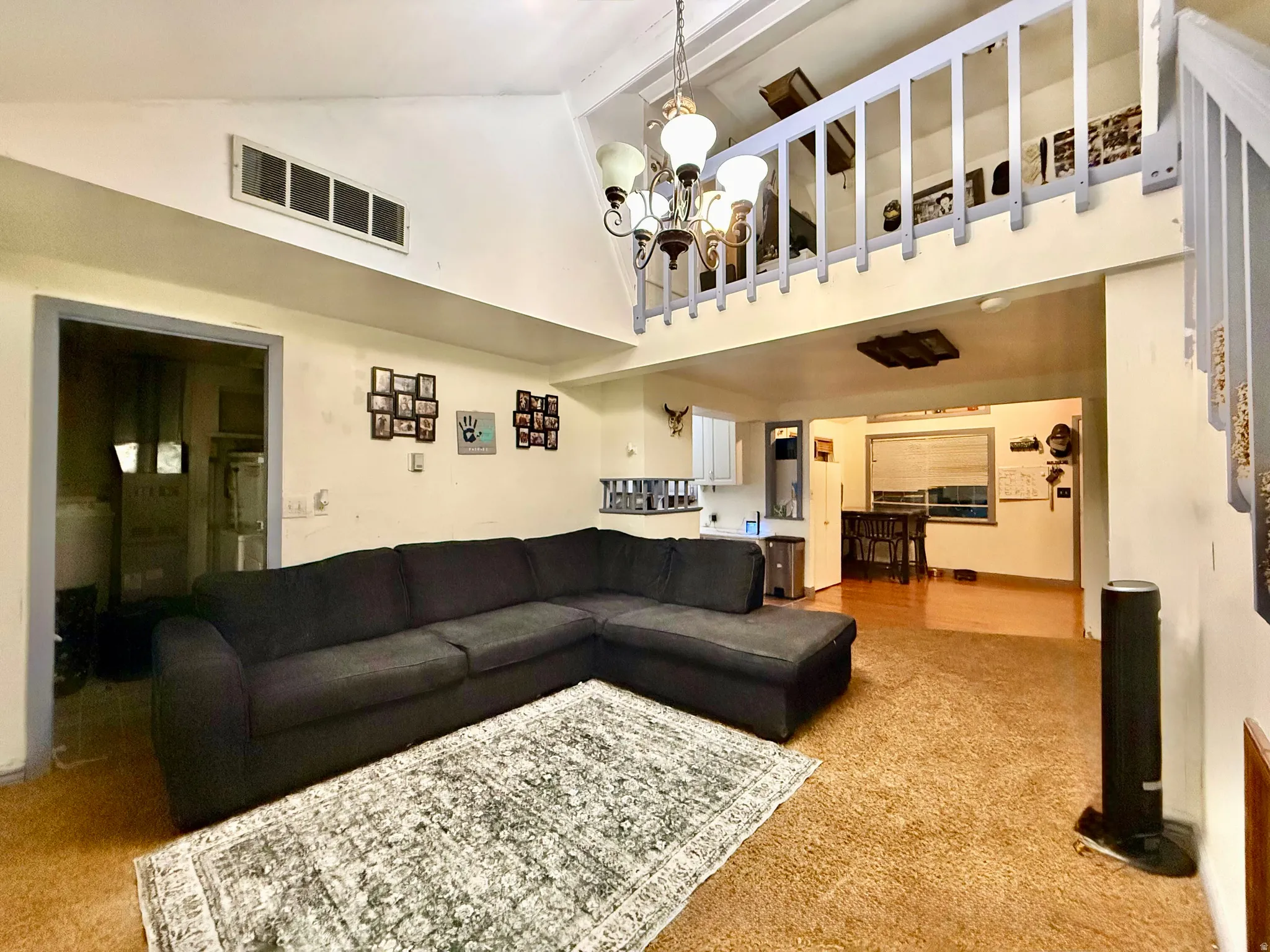 Vaulted ceiling with exposed beams, decorative chandelier, and a loft space with a wood railing