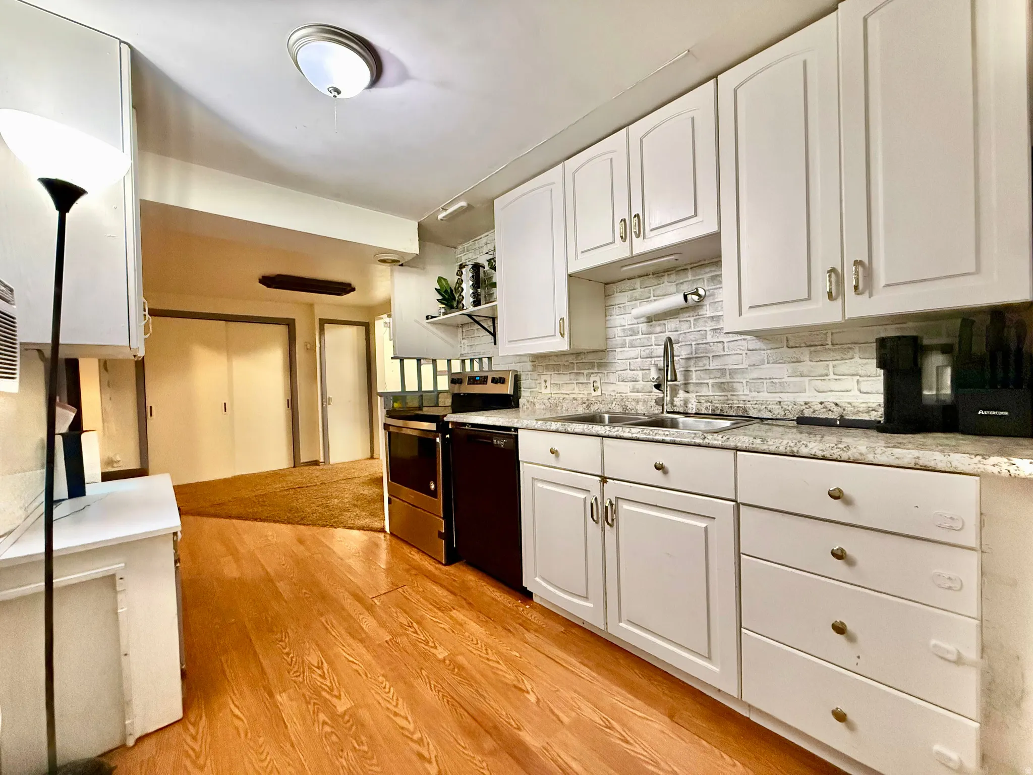White cabinetry with gold-tone hardware, a stainless steel sink, a light-toned countertop, and wood-finish flooring