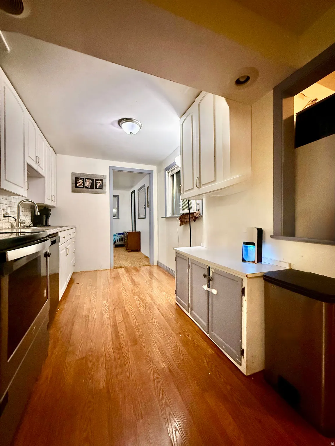 Kitchen featuring wood-finish flooring, white cabinetry, a subway tile backsplash, and stainless steel appliances