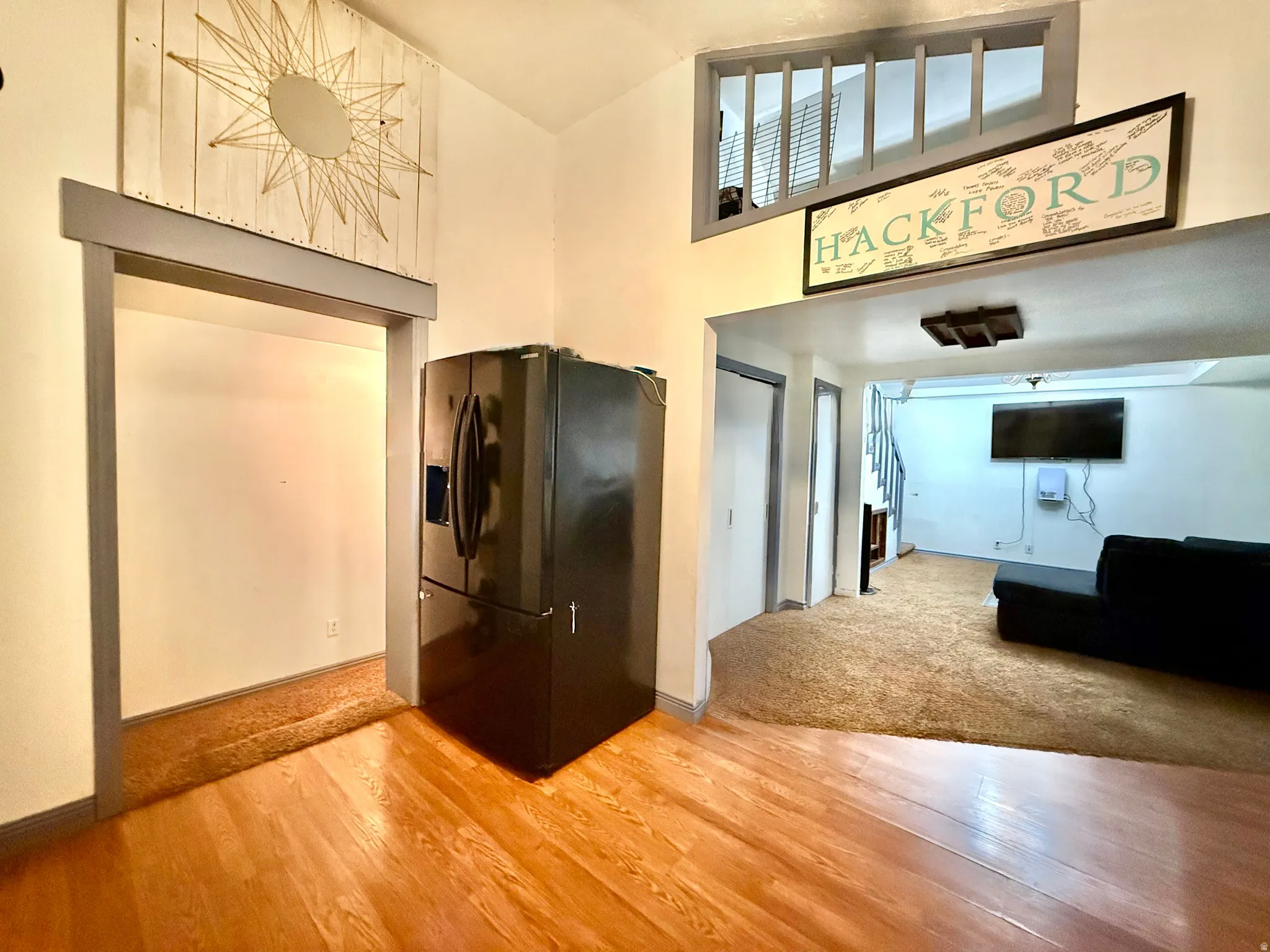 Open floor plan with warm wood-finish flooring, stainless steel refrigerator, and abundant natural light from transom windows