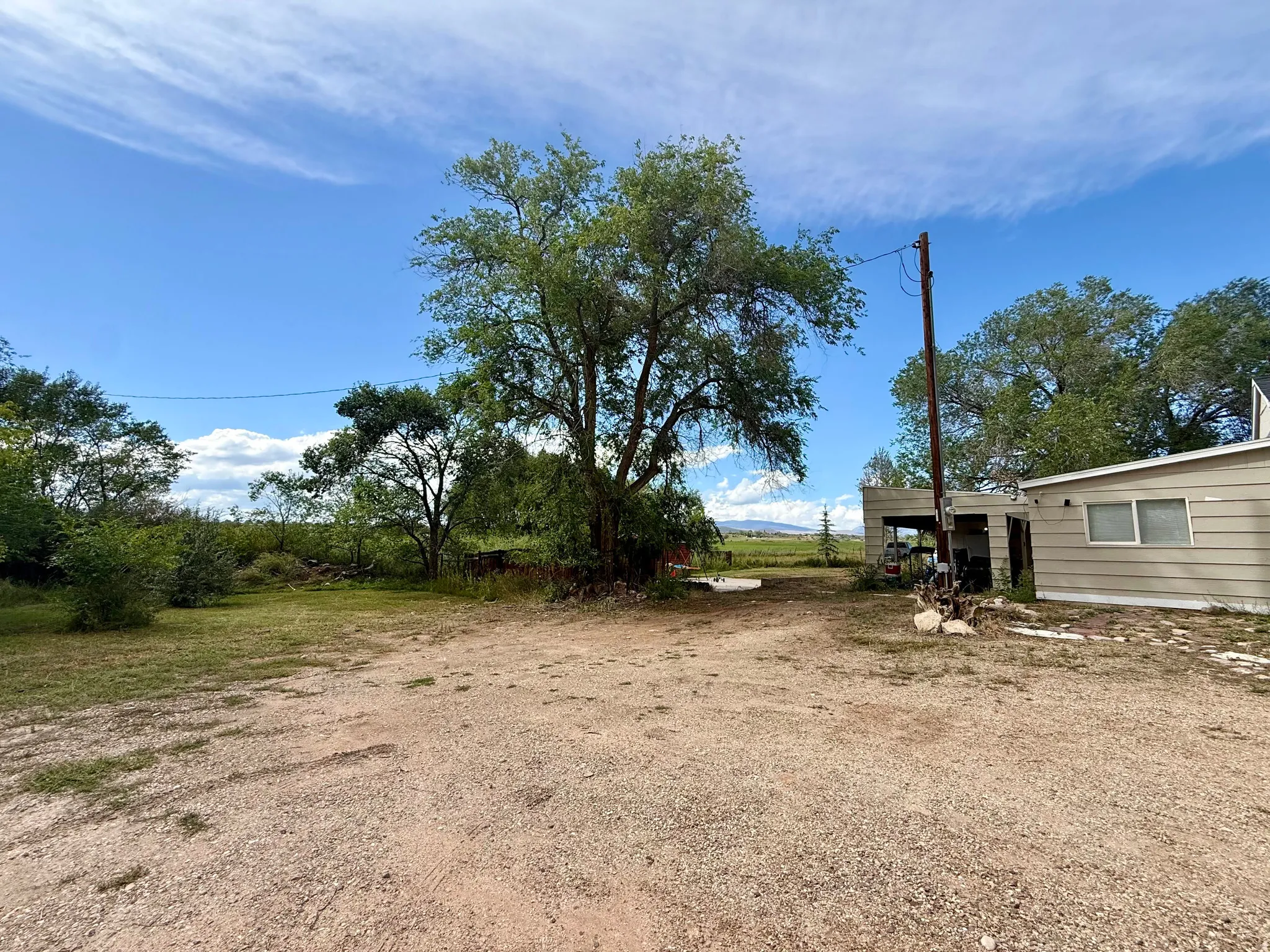 Gravel lot with mature trees and a single-story structure with horizontal siding