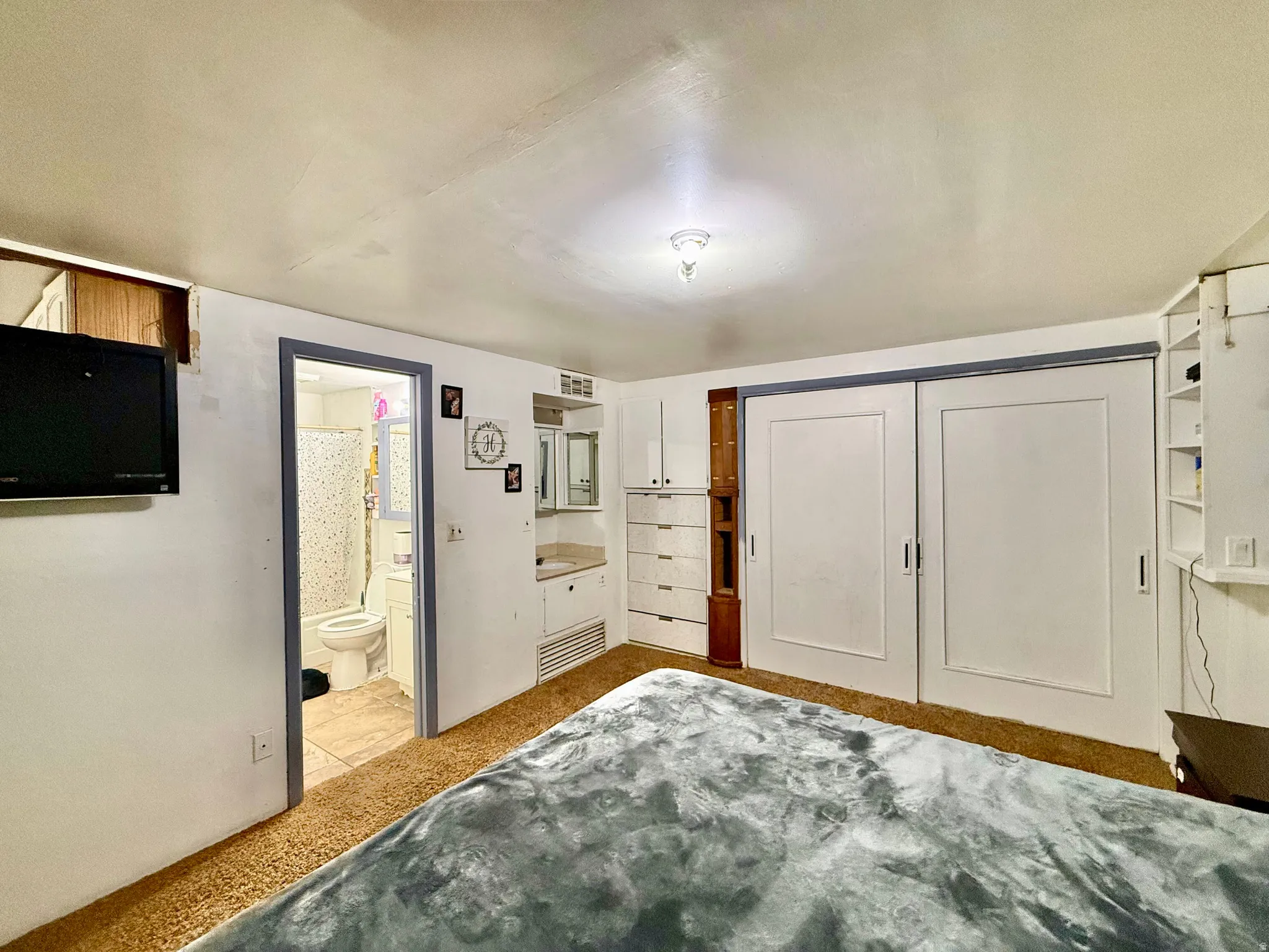 Wall-mounted television, built-in storage shelving, built-in vanity with mirror, and sliding closet doors