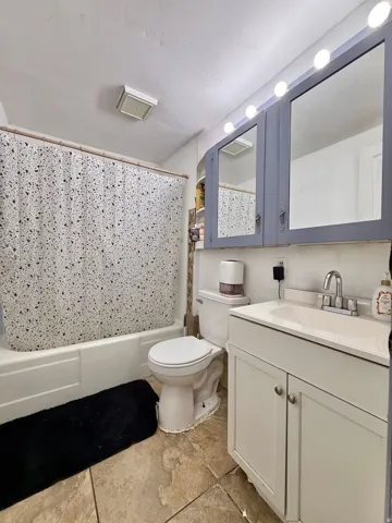 Tile flooring, white vanity with integrated sink, chrome-finish faucet, built-in medicine cabinet with mirror, bathtub with shower