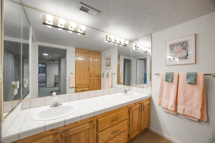 Dual vanity with integrated sinks, tile countertop, and wood-finish cabinetry