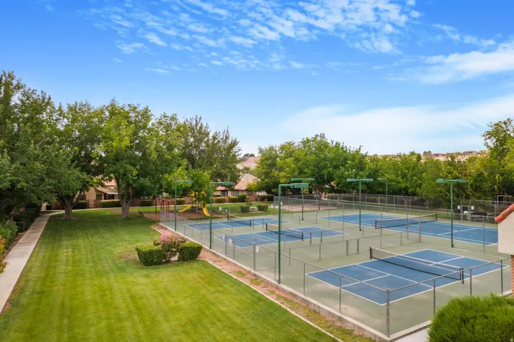 Multiple fenced tennis courts, expansive green lawn, mature trees, paved pathway, and a playground structure