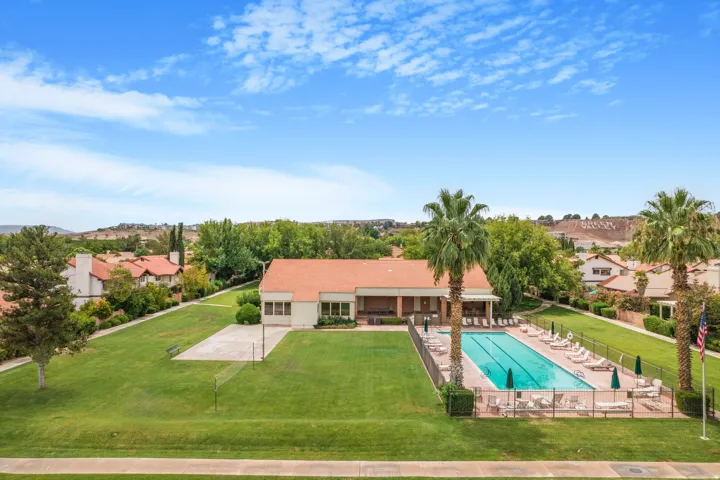 Expansive swimming pool with surrounding fencing, adjacent recreation building, and green spaces
