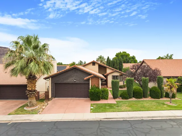 Property exterior with a tile roof, an attached garage, a paved driveway, and mature landscaping
