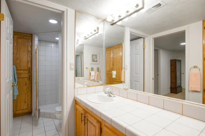 Vanity with wood-finish cabinetry, tile countertop, and integrated sink