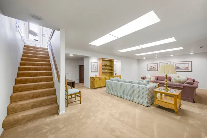 Carpeted stairway leading to a spacious room with recessed lighting and built-in shelving