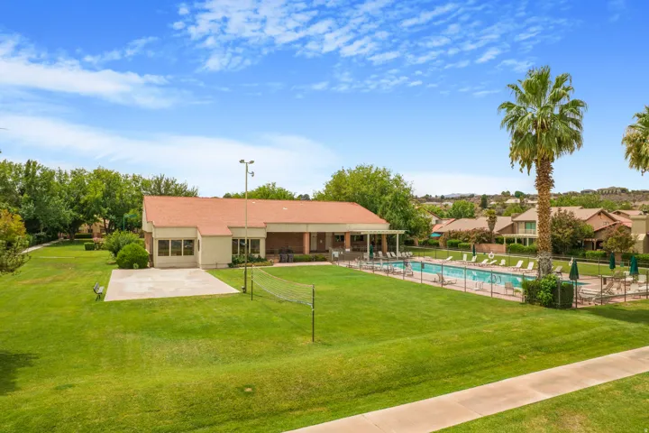 Outdoor swimming pool, fenced pool deck with lounge chairs, adjacent clubhouse with covered patio, grass recreation area, and mature landscaping