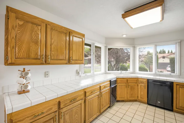 Kitchen featuring wood cabinetry, white tile countertops, white tile flooring, and integrated black appliances