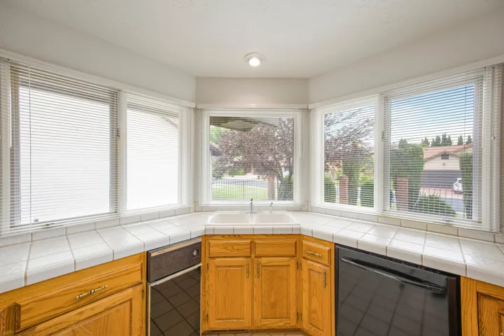 Bay window with integrated double basin sink, white tile countertops, and wood cabinetry