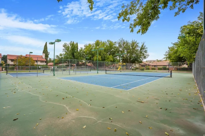 Tennis court with blue playing surface, surrounding green court area, and chain-link fencing
