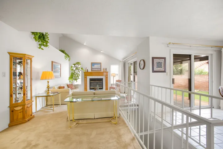 Vaulted ceiling, fireplace with wood mantel, sliding glass doors, upper wall ledge, and white railing