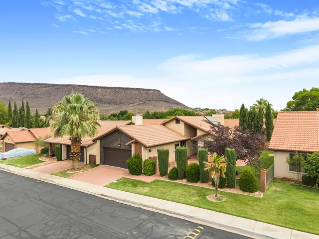 Terracotta tile roofs, stucco exterior finish, attached garage, paved driveway, and mature landscaping