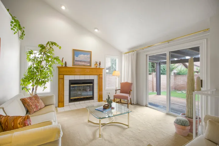 Vaulted ceiling, recessed lighting, fireplace with tile surround and wood mantel, sliding glass door, and backyard access with deck
