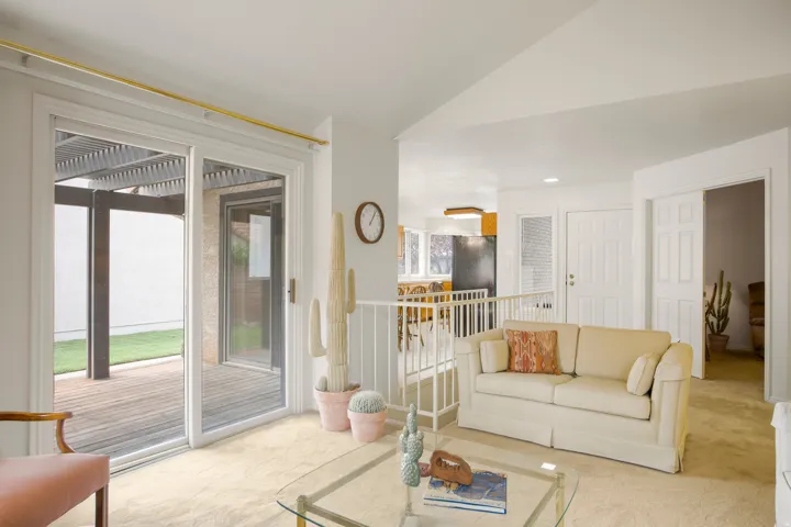 Sliding glass doors opening to an exterior wood deck with a pergola, carpeted flooring, and a half-wall partition with railing