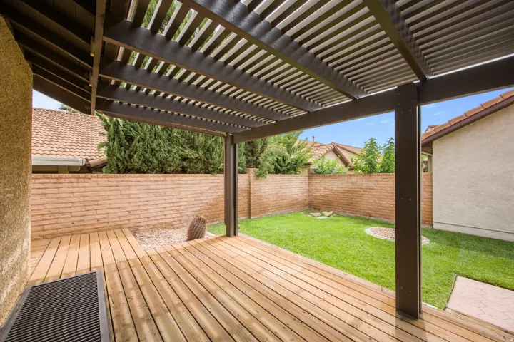 Wood-finish deck with a patio cover, enclosed by a brick wall, featuring a grass lawn