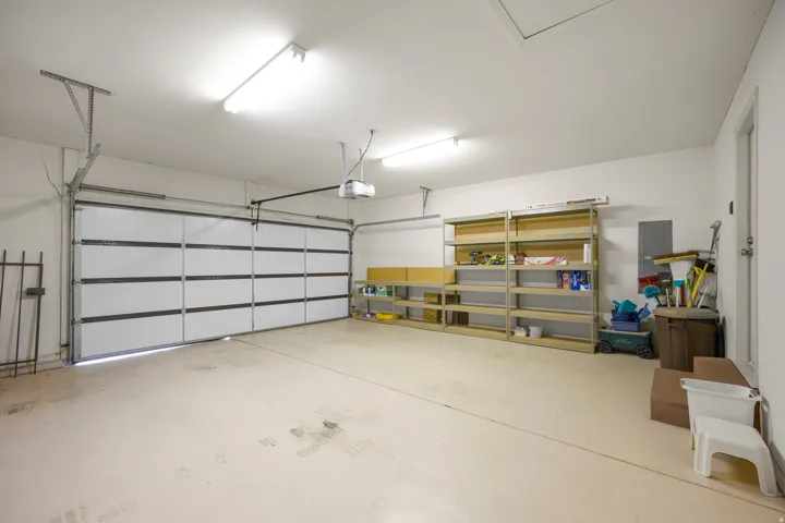 Spacious garage with a sectional overhead door, automatic opener, built-in shelving, and overhead fluorescent lighting