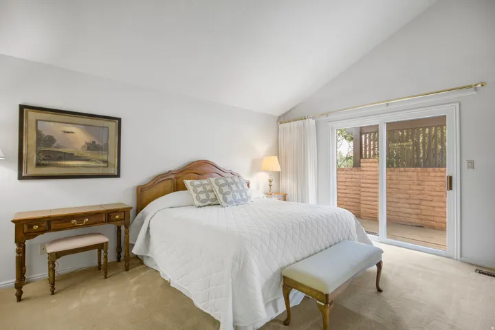 Vaulted ceiling, sliding glass door, private patio with block wall, carpeted flooring, and a decorative wood headboard
