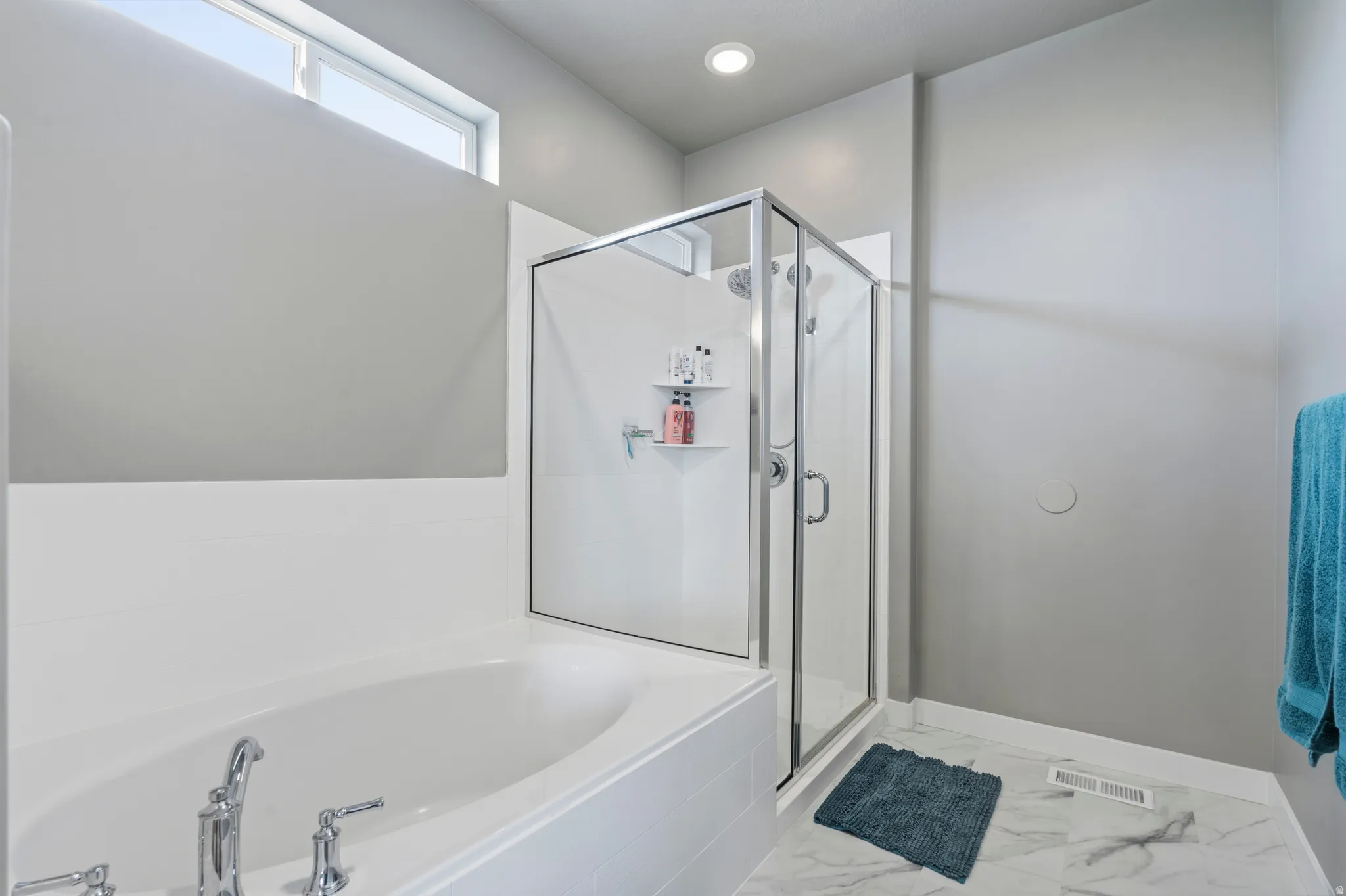 Soaking tub with chrome fixtures and an adjacent glass-enclosed shower featuring a built-in shower caddy