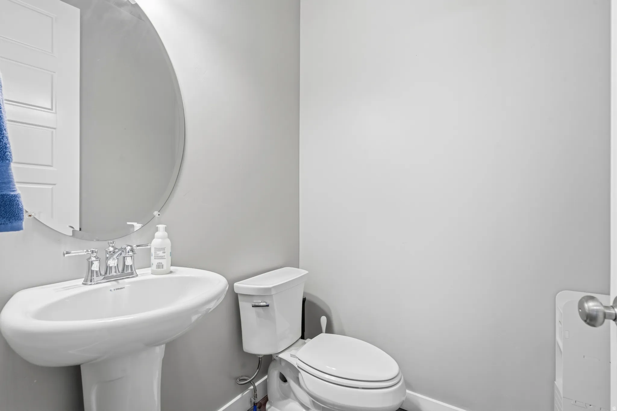 Pedestal sink with chrome faucet, oval frameless mirror, and a white two-piece toilet