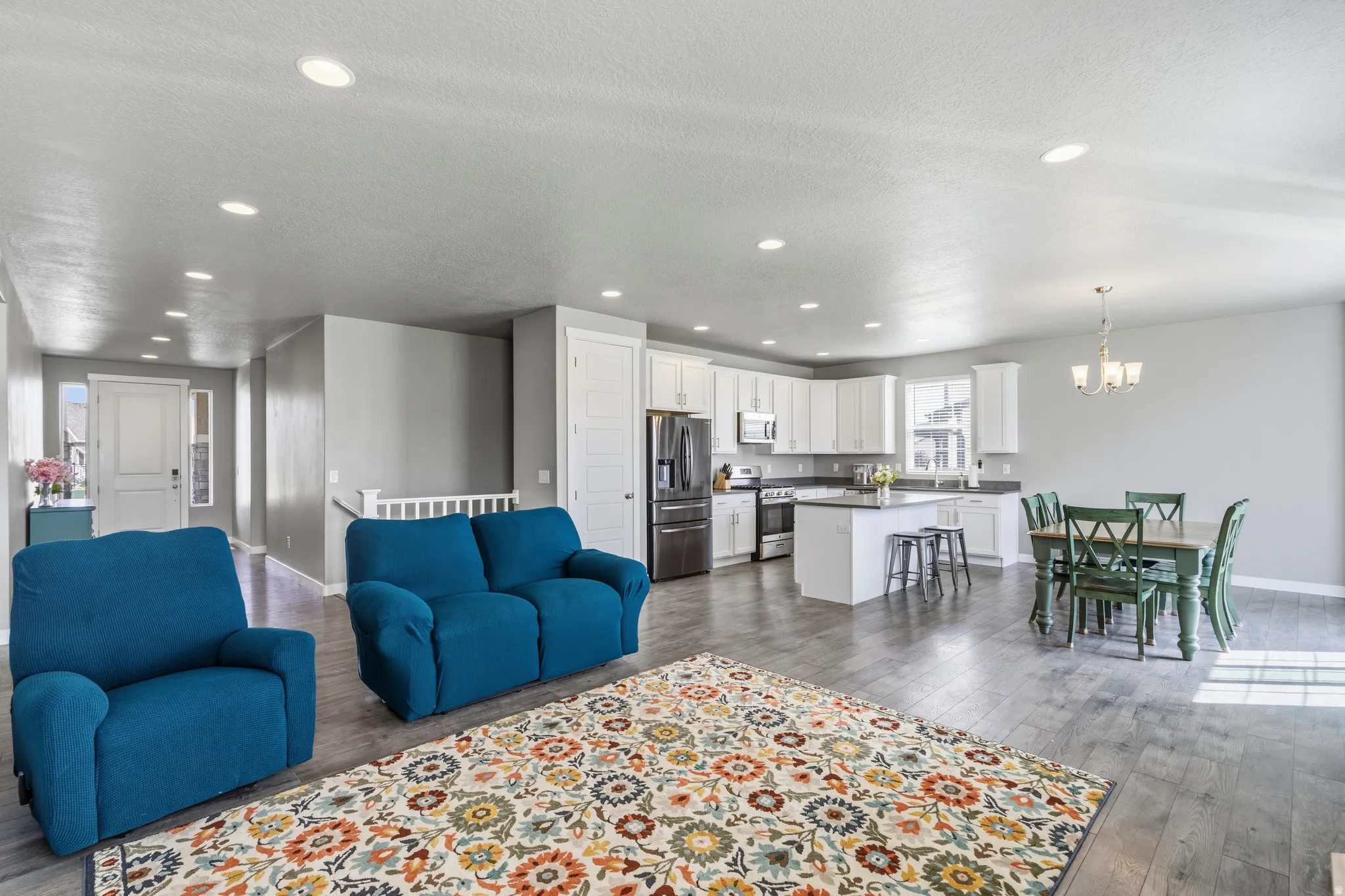 Open-concept living area featuring wood-finish flooring, recessed lighting, and a kitchen with white cabinetry, a central island, and stainless steel appliances