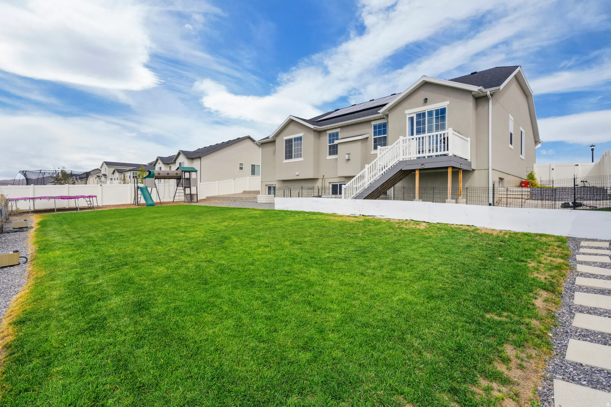 Expansive manicured lawn with mature landscaping, stone pathway, and composite deck with metal railings