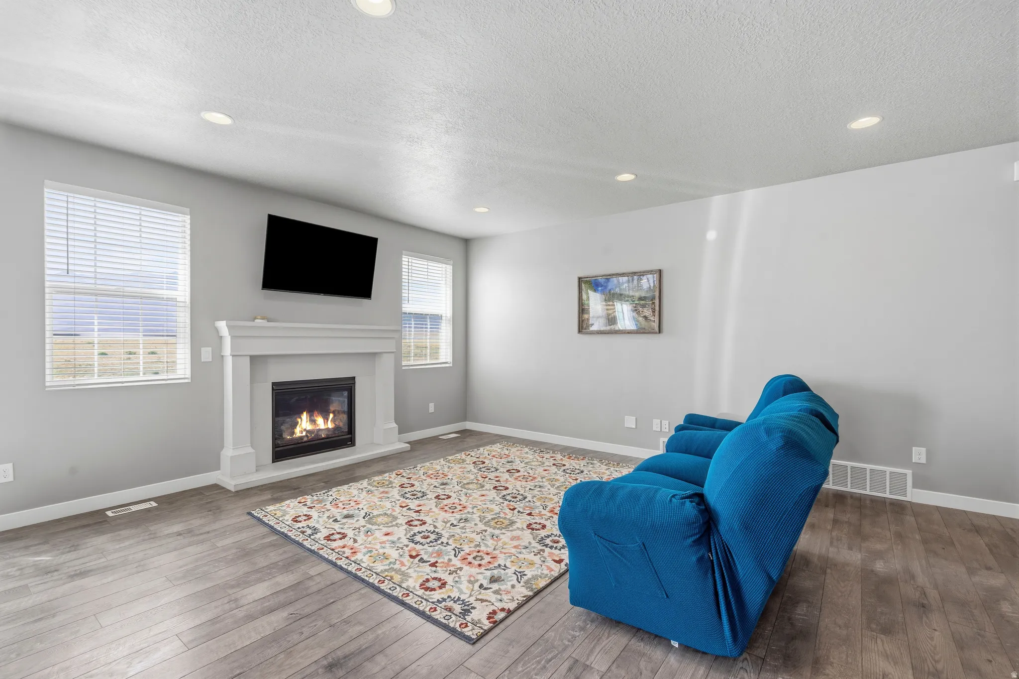 Living area featuring wood-finish flooring, recessed lighting, and a fireplace with a white mantel