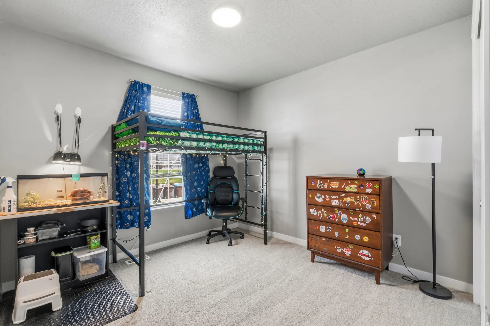 Versatile bedroom featuring a lofted sleeping area with blue curtain accents, wood-finish flooring throughout, recessed ceiling lighting, and ample space for multiple functional zones