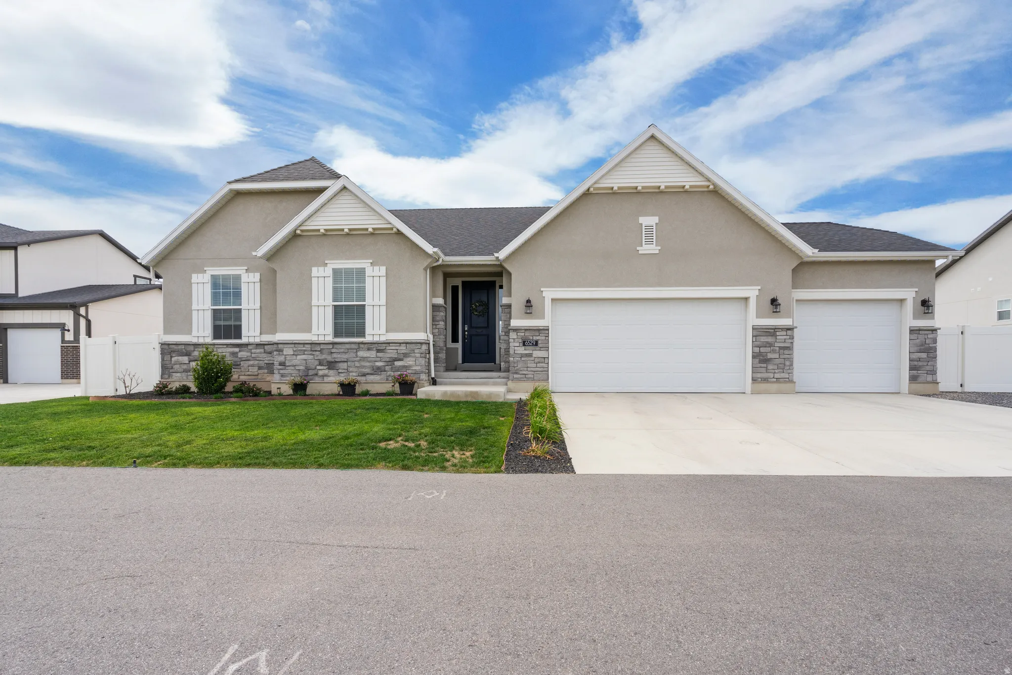 Stucco exterior with stone accenting, dark shingle roof, white window shutters, and a two-car garage