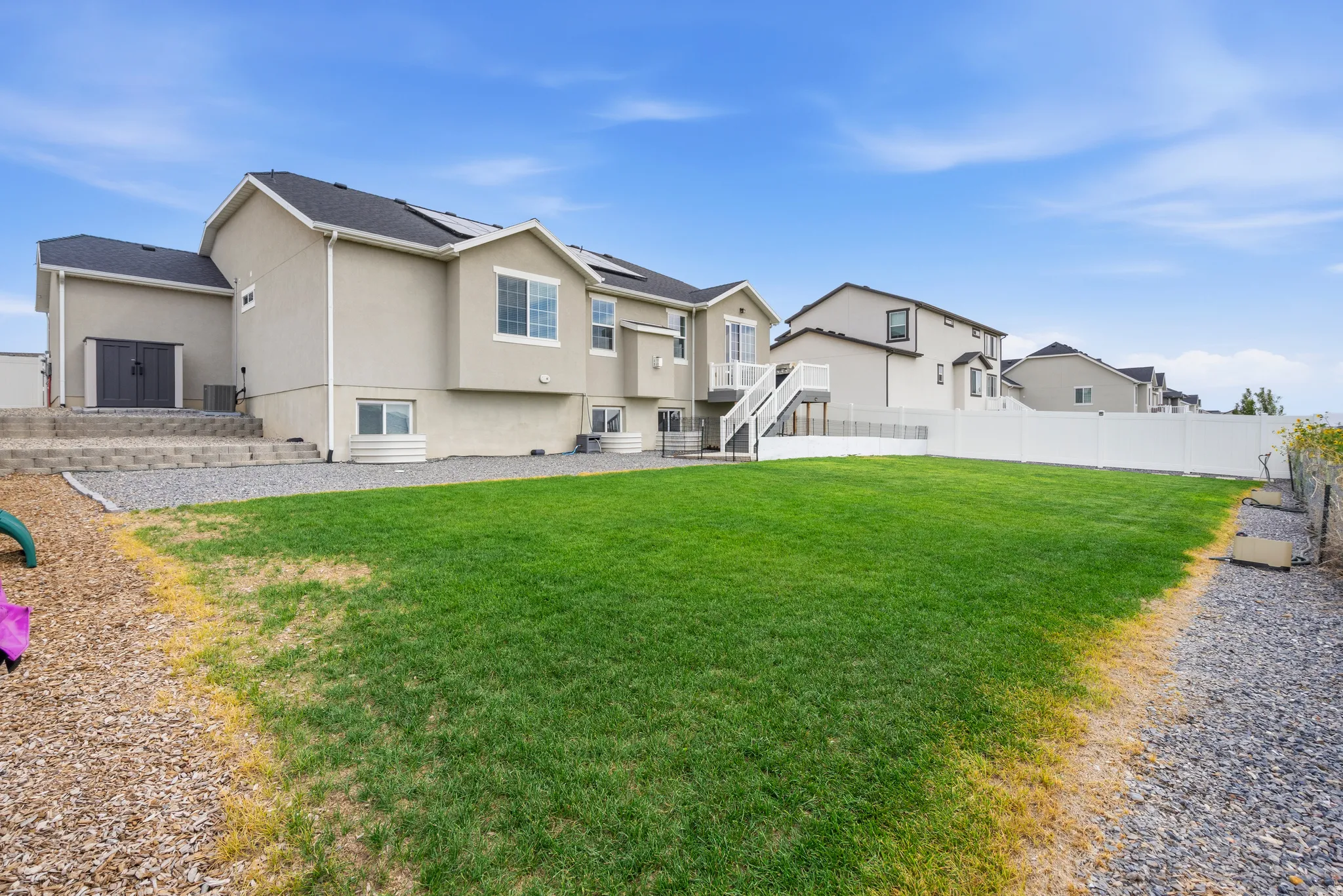 Expansive backyard featuring a manicured lawn, white vinyl fencing, and a gravel pathway