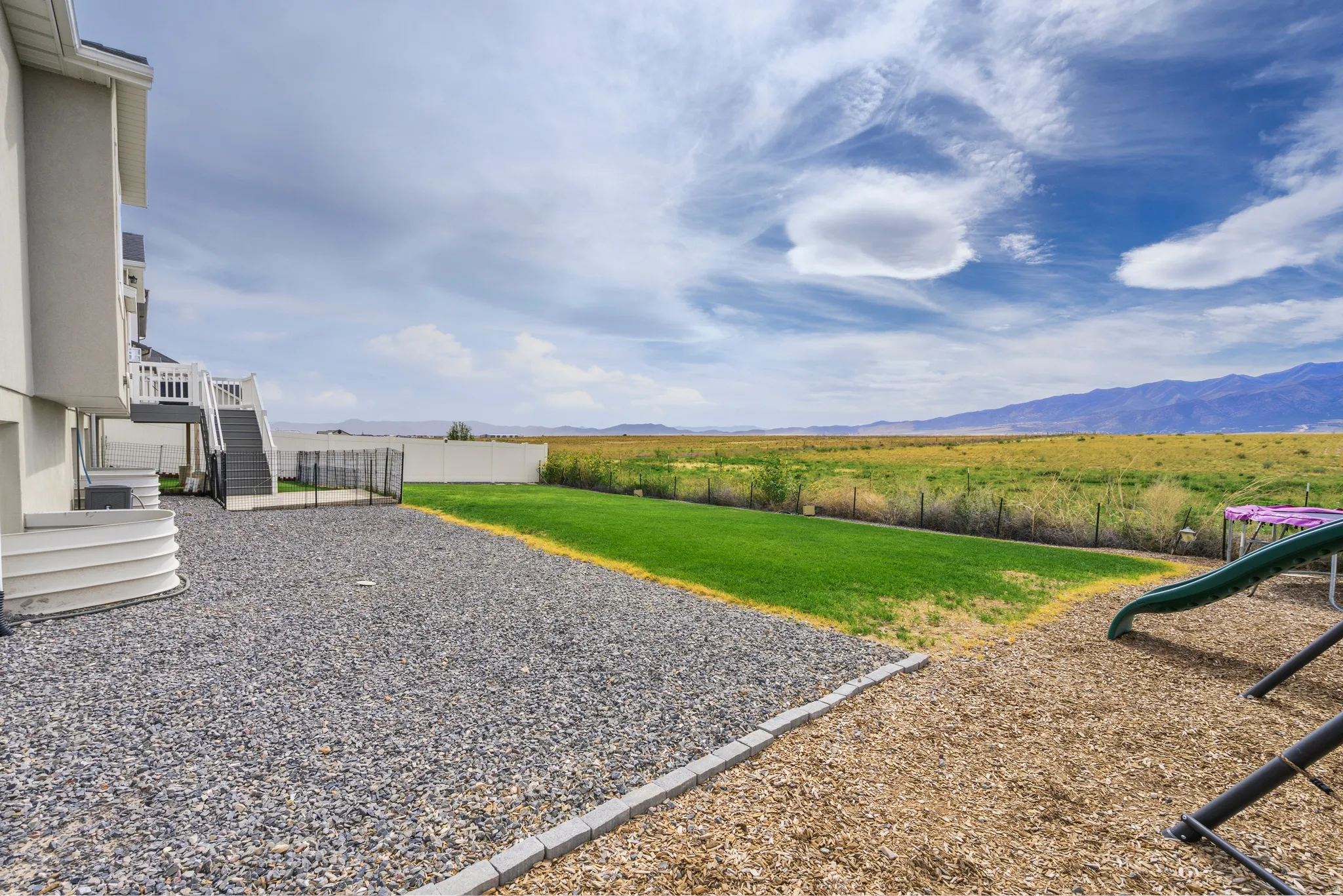 Expansive backyard featuring a gravel and wood chip ground cover, a manicured lawn, and a white privacy fence