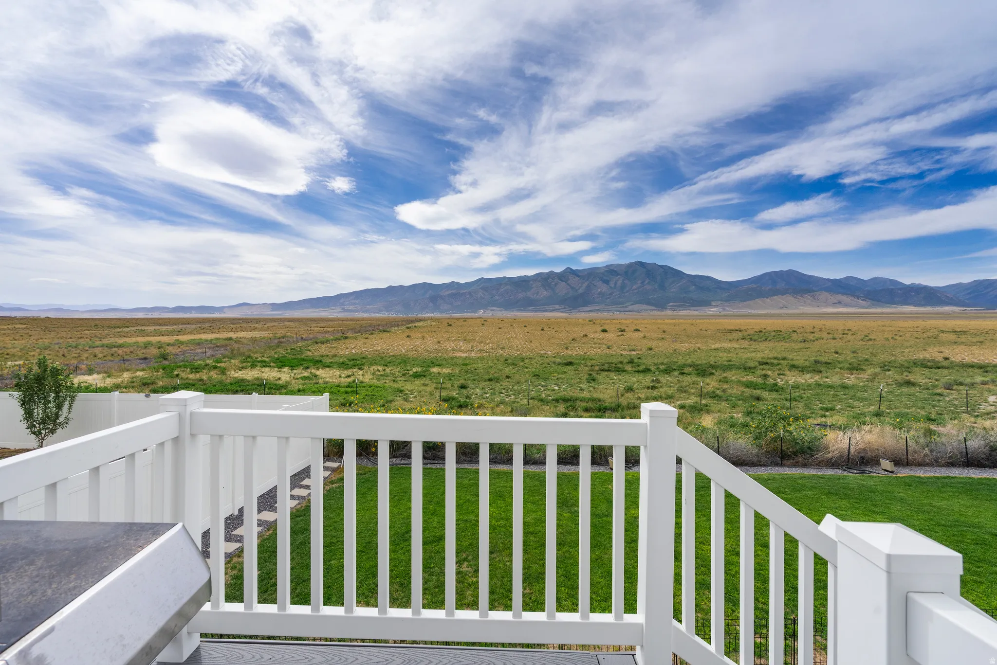 Expansive mountain range backdrop, vast natural landscape, groomed lawn, white privacy fencing, and a durable deck railing