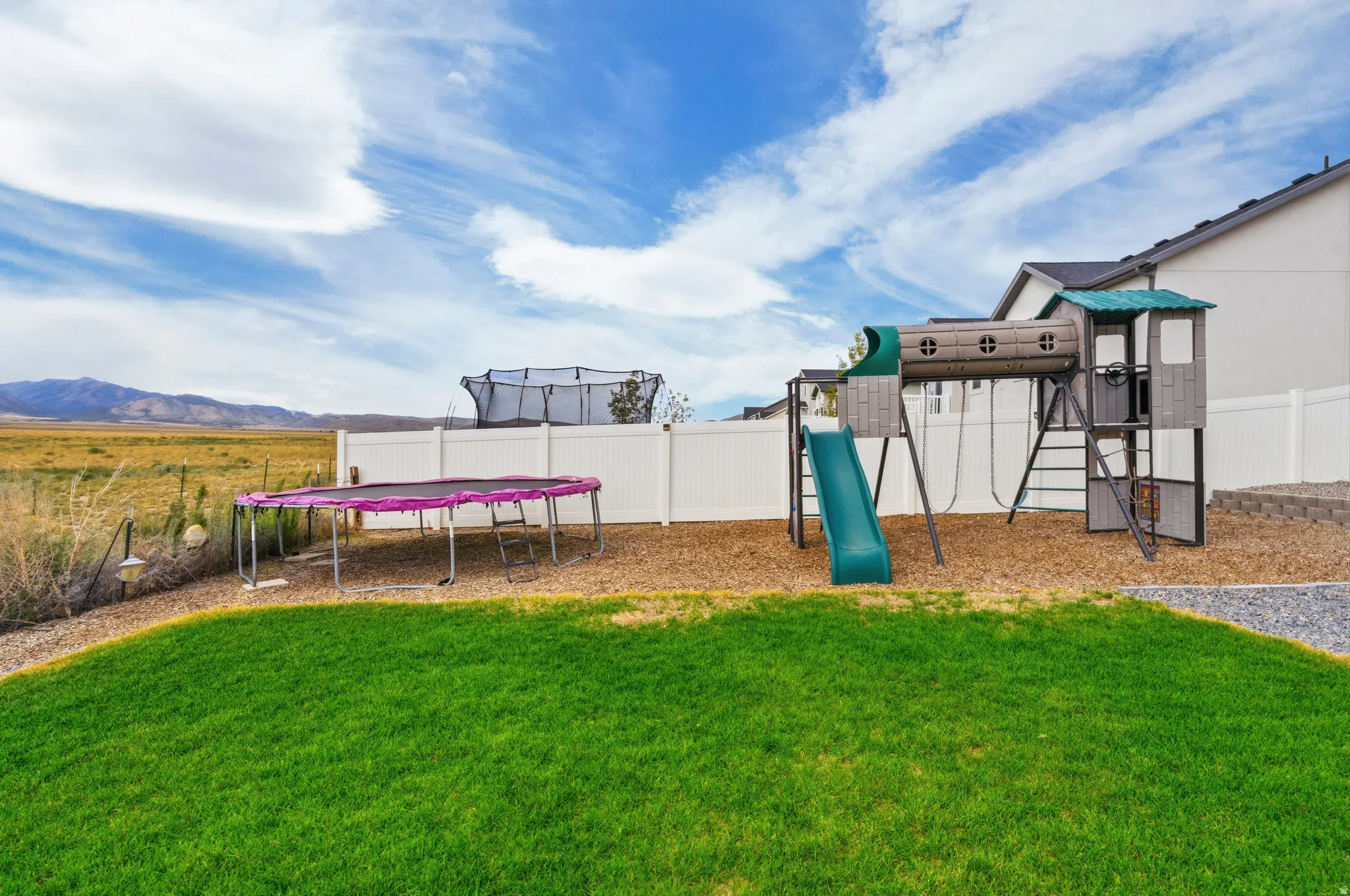 Expansive backyard featuring a manicured lawn, white privacy fencing, and a built-in playset with slide