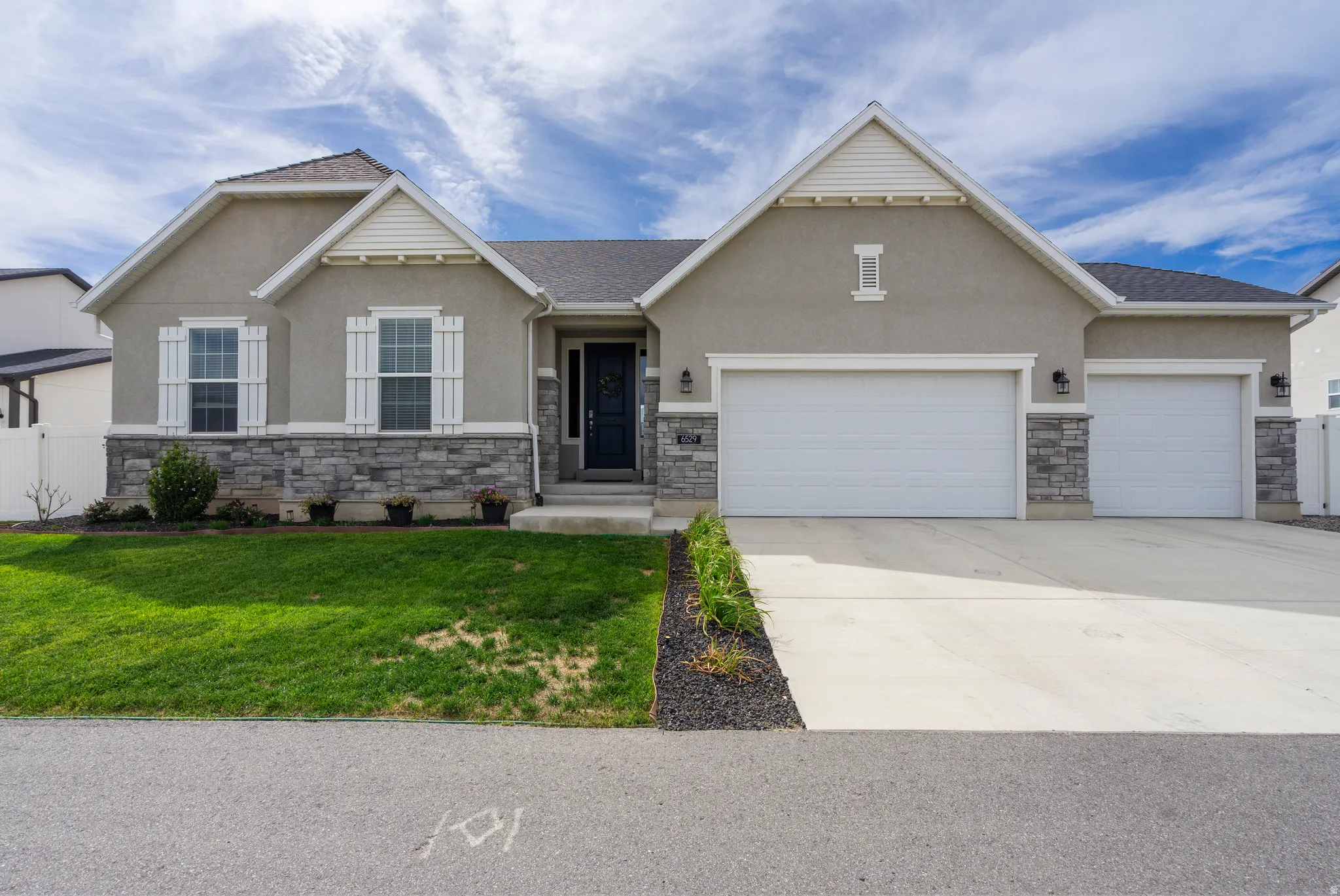 Stucco exterior with stone veneer accents, multiple white garage doors, white window shutters, and a dark entry door