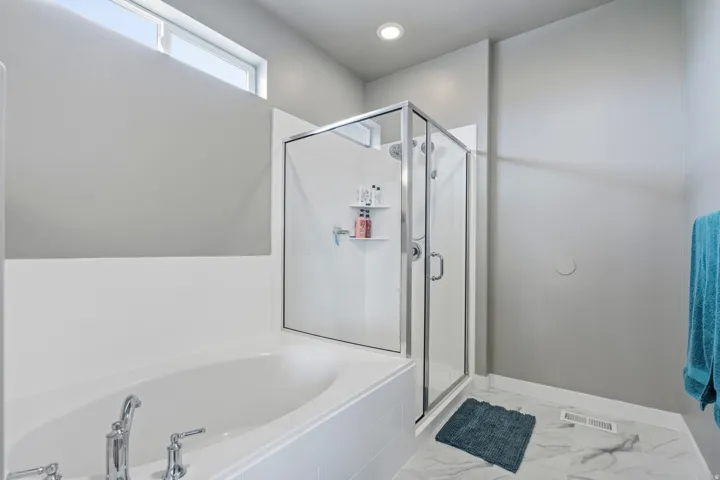 Soaking tub with chrome fixtures and an adjacent glass-enclosed shower featuring a built-in shower caddy